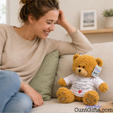 A smiling woman sits on a beige couch next to a plush teddy bear wearing a white shirt that says 'Cuntly McCunface.' The bear has a visible Cuntly Gifts tag, and the photo is taken in a bright, neutral indoor setting.